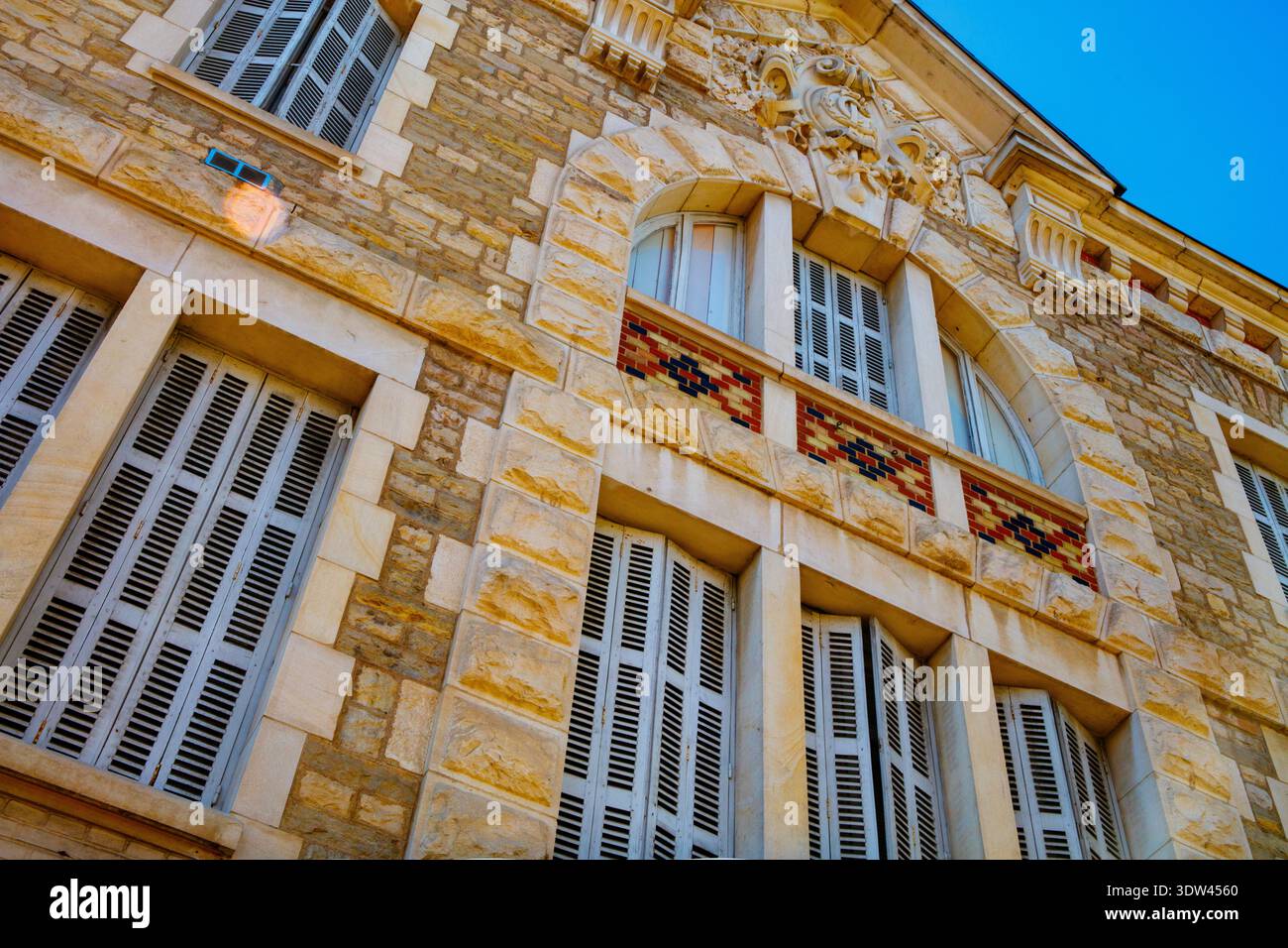 Una vista dettagliata della facciata di un edificio storico che mostra intricati lavori in pietra e finestre con persiane. Foto Stock