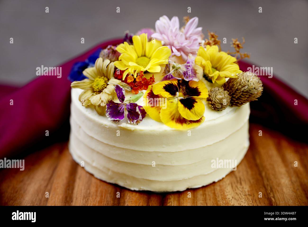 Elegante torta color crema bianca decorata con vivaci fiori commestibili Foto Stock