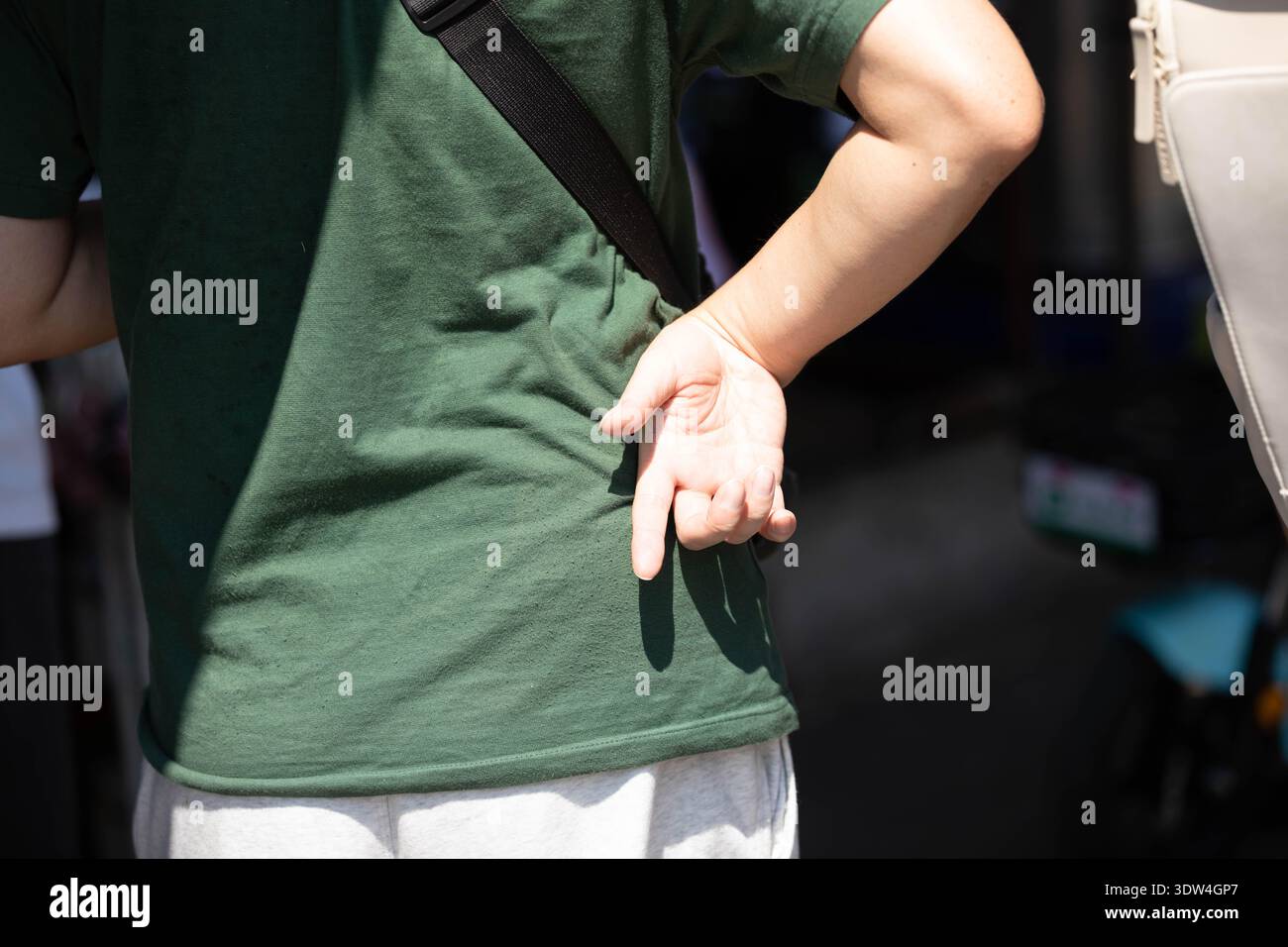 Uomo con t-shirt verde in piedi con la mano sull'anca, da solo nella folla, persona solitaria in strada trafficata, texture della pelle della mano, primo piano, al Chatuchak Market. Foto Stock