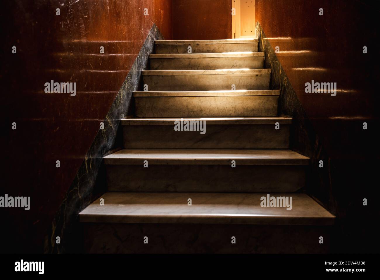 Scala in marmo illuminata dal sole in un vecchio edificio romano con riflessi su pareti marroni lucide e un delicato contrasto di luce e ombra Foto Stock