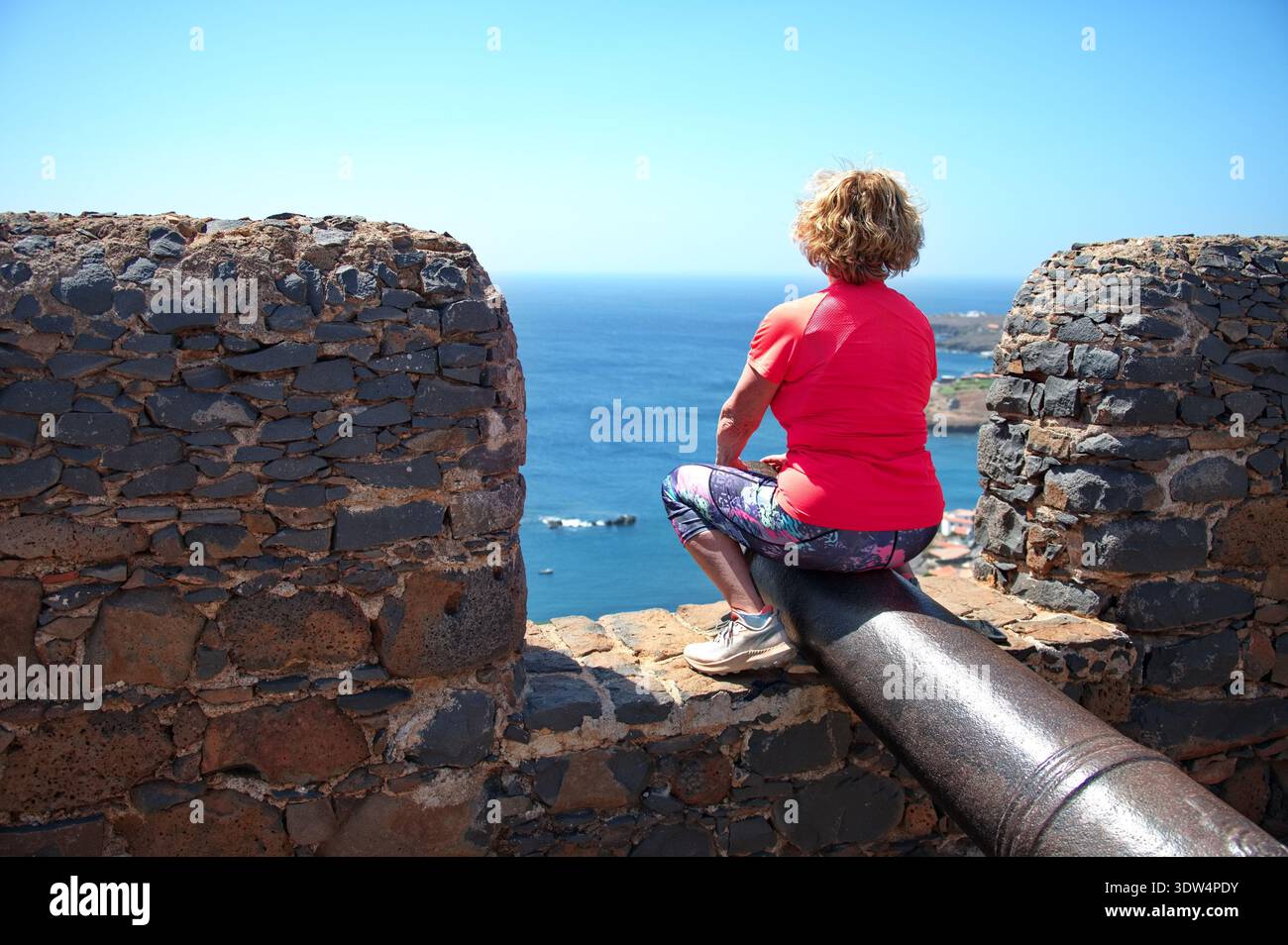 Donna anziana seduta su una pistola sulla fortezza di Capo Verde Foto Stock