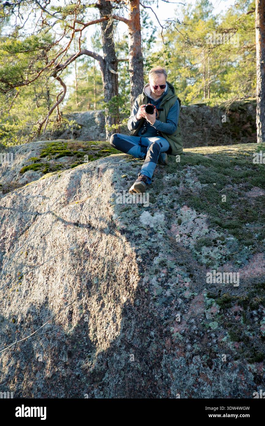 Il creatore di contenuti di viaggio filma video di avventura con fotocamera sulla scogliera della foresta in Finlandia. Stile di vita all'aperto, nomade digitale Foto Stock
