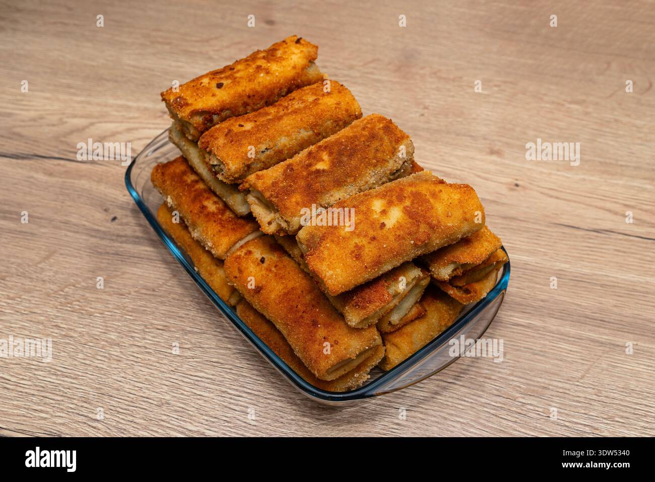 Crocchette polacche fritte con impanatura croccante impilate in una teglia da forno in vetro trasparente Foto Stock