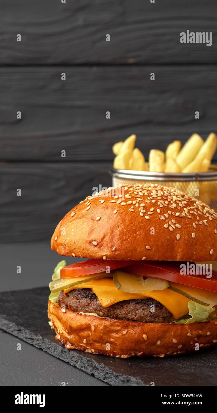 Hamburger fresco con lattuga al formaggio e pomodoro servito con patatine fritte su un tavolo scuro Foto Stock