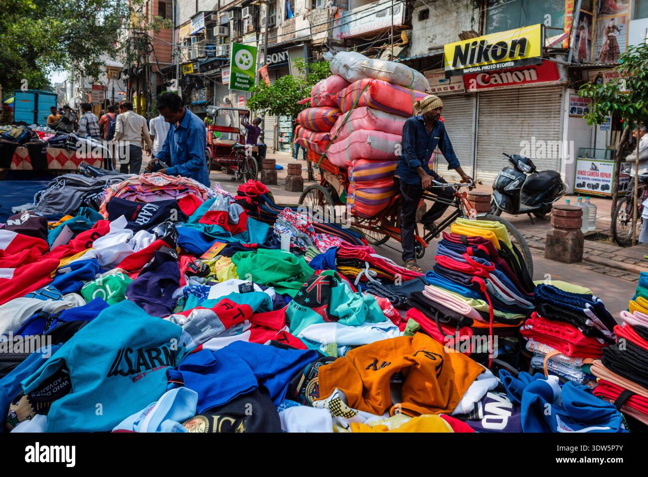 Mercato di strada a Chandni Chowk, Vecchia Delhi. Un uomo fa un giro in risciò carico di sacchi e passa davanti a bancarelle di vestiti colorati. Nuova Delhi, capitale nazionale, Terri Foto Stock