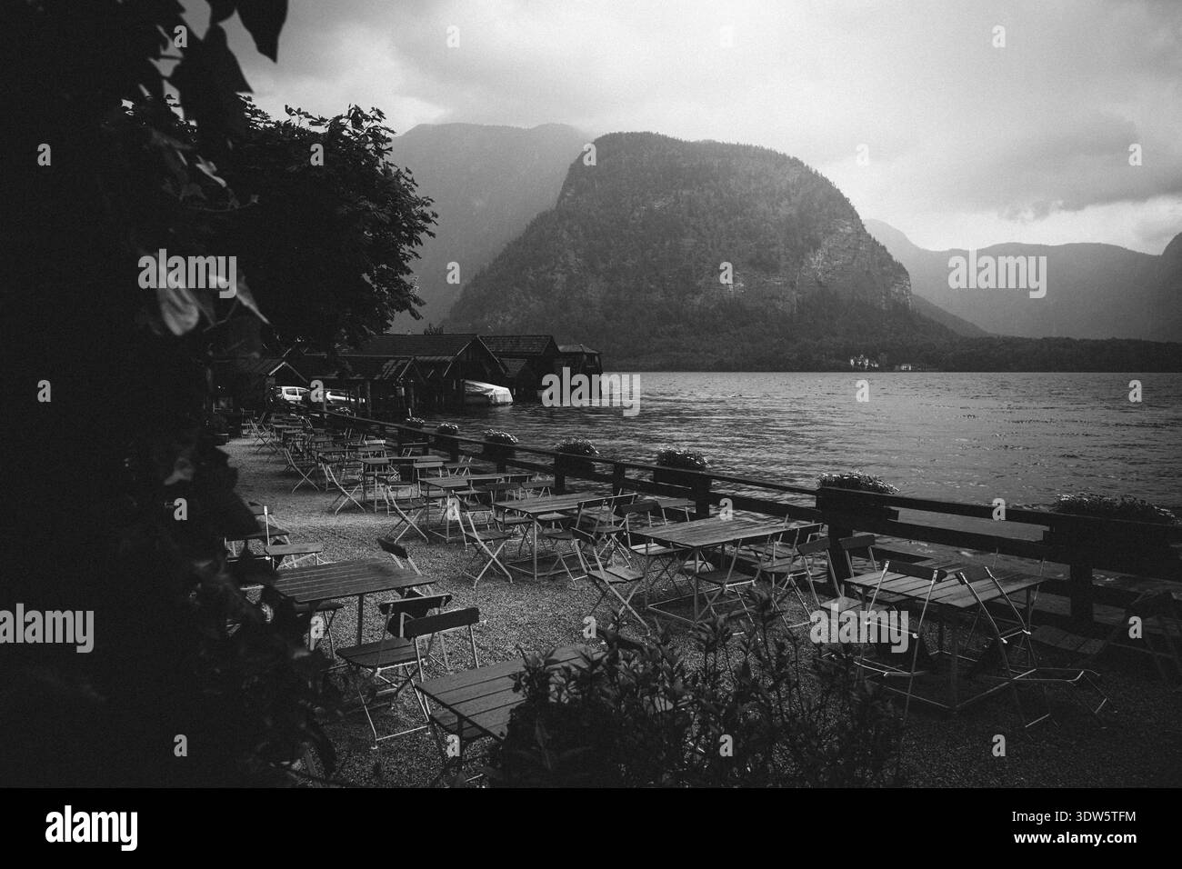 Tavoli da caffe' vuoti all'aperto vicino ad un tranquillo lago con spettacolari montagne sullo sfondo Foto Stock