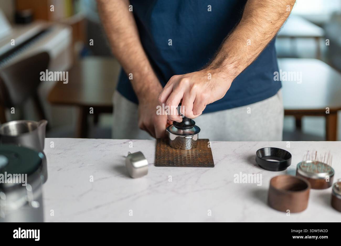Un primo piano mostra un uomo adulto che usa una manomissione per premere i fondi di caffè in un portafiltro durante la preparazione dell'espresso. L'immagine evidenzia la precisione, t Foto Stock