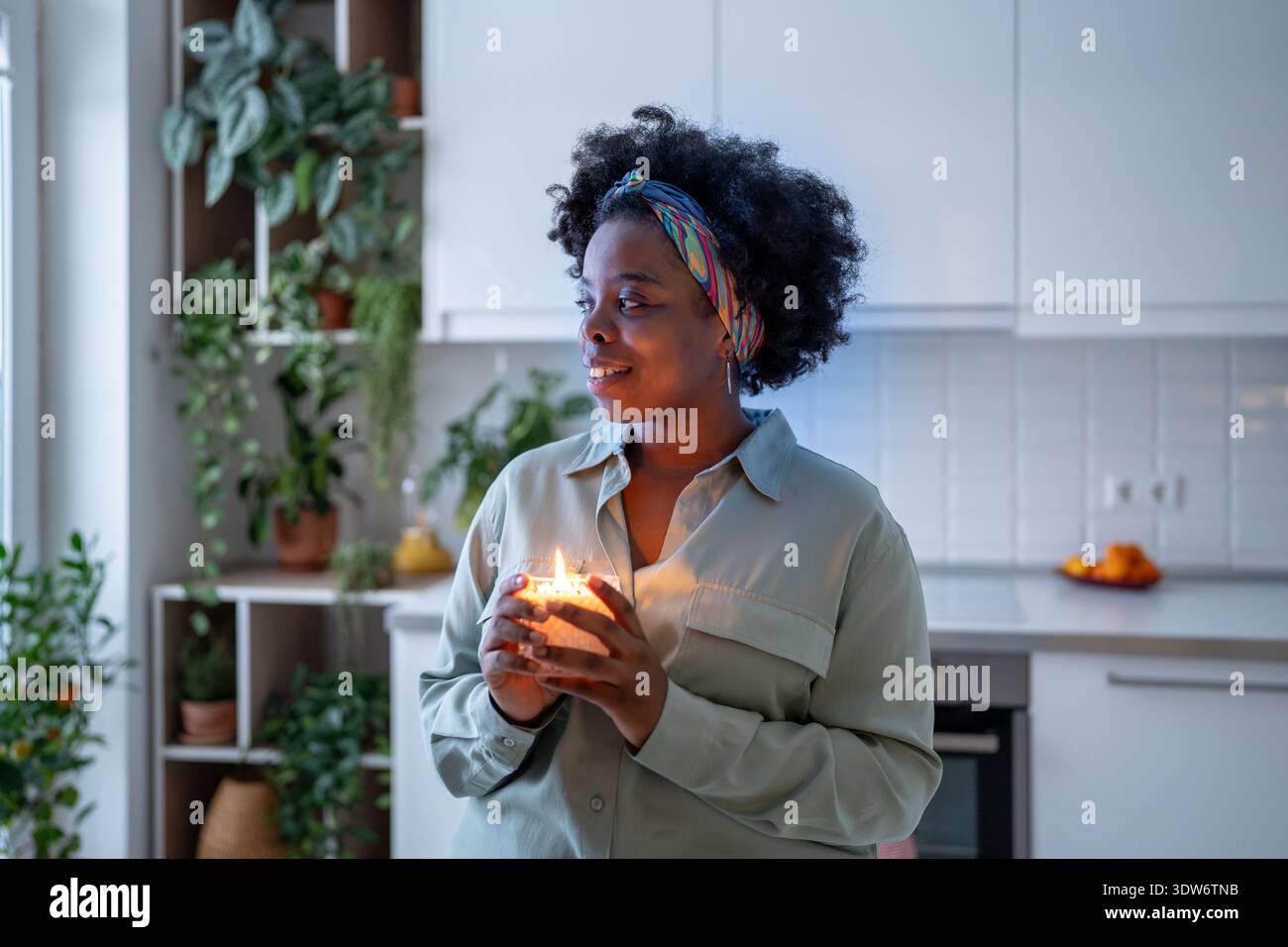 Una donna nera serena e contenta che accende una candela profumata sente gratitudine e gode di un'atmosfera accogliente a casa. Tempo per me. Foto Stock