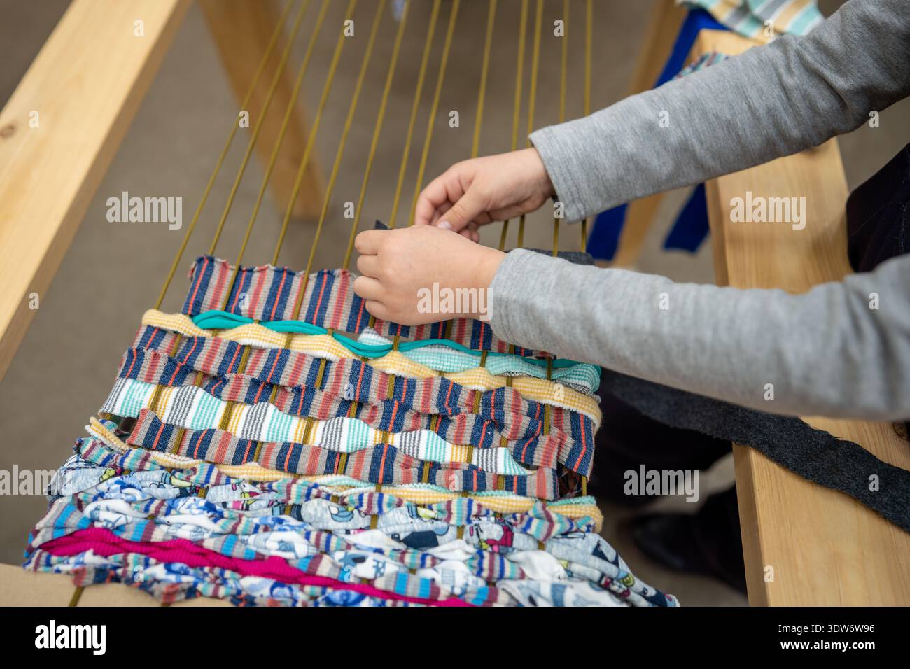 Tessitura . Le mani dei bambini da primo piano tessono con cura i fili sul telaio nello studio dei laboratori artigianali tradizionali. Foto Stock