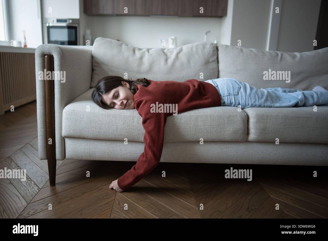 Una donna rilassata si riposa a casa e si gode un sonnellino pomeridiano, dormendo a faccia in giù su un comodo divano. Recupero da fatica Foto Stock