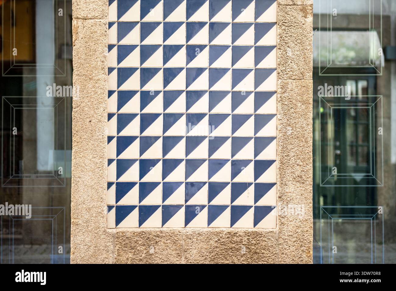 Primo piano delle tradizionali piastrelle azulejo portoghesi a Porto, Portogallo, caratterizzato da un motivo geometrico blu e bianco incorniciato da pietra testurizzata e riflettente Foto Stock
