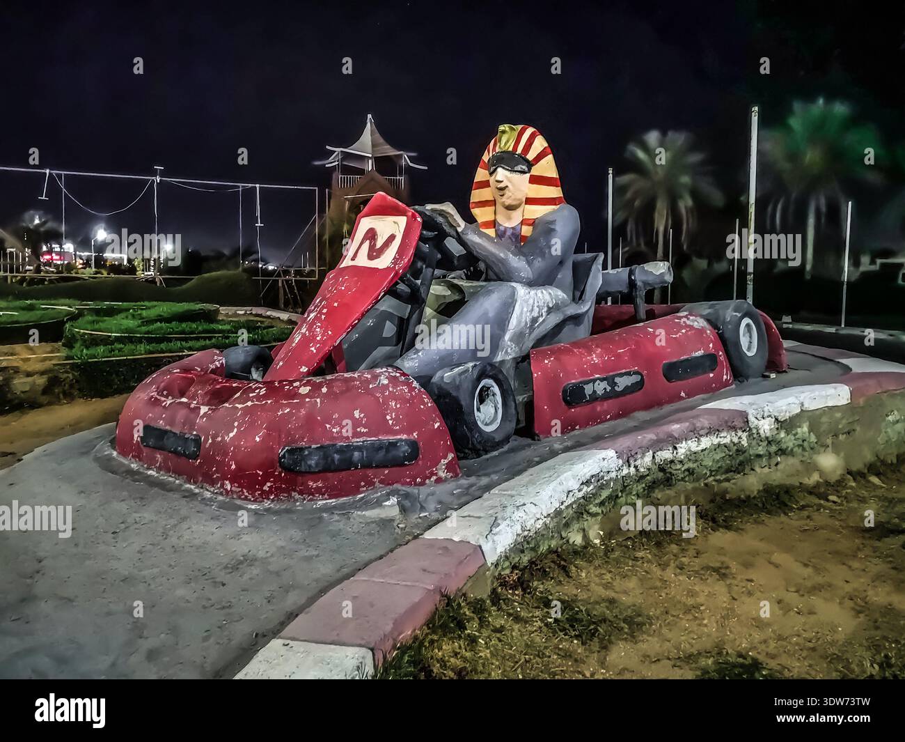 Sharm El Sheikh, Egitto - 20 gennaio 2020: Statua del faraone alla guida di un'auto da corsa a Sharm El Sheikh di notte. Vecchia scultura squallida in un resort egiziano - Immagine stock catturata con smartphone