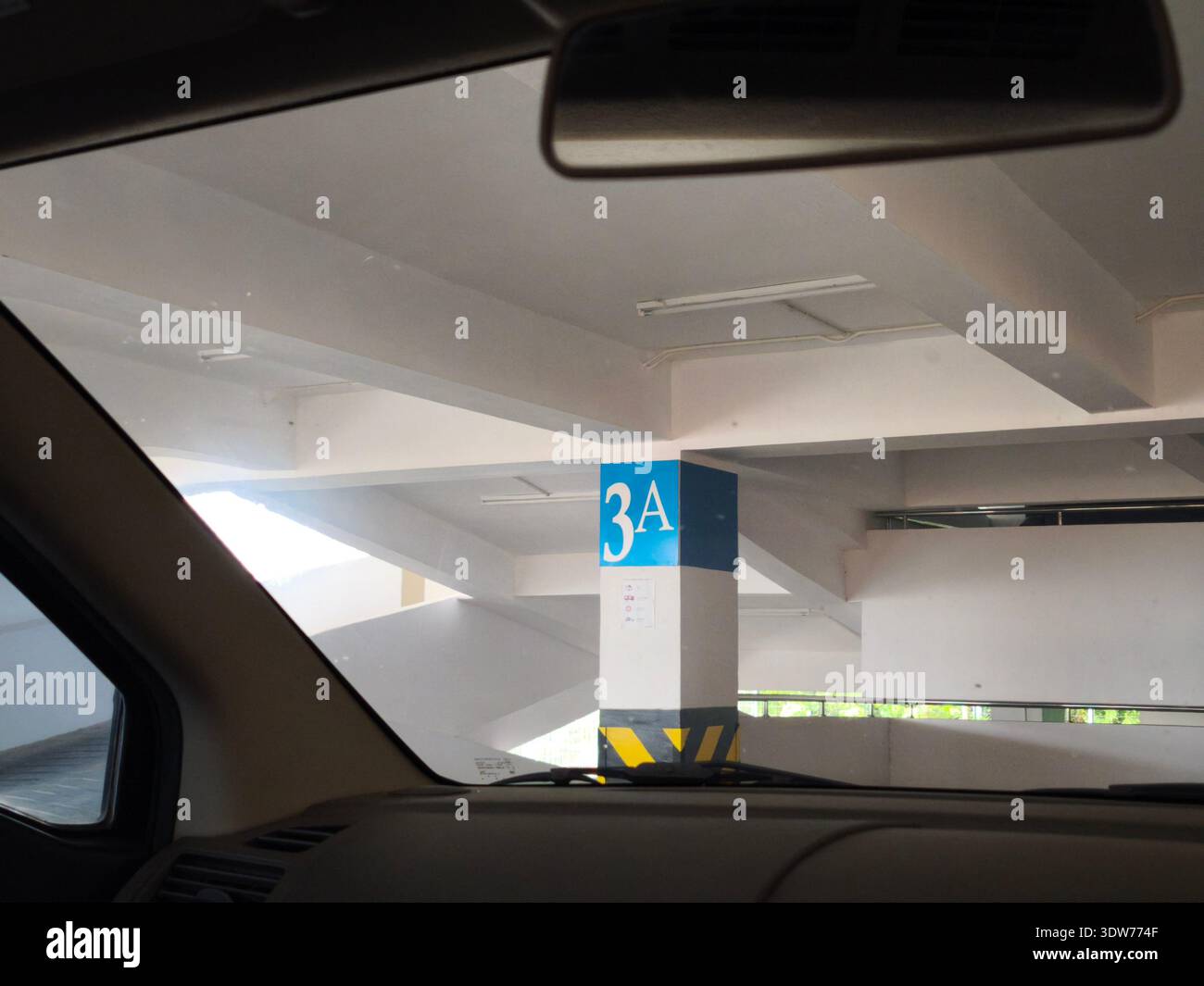 Vista dall'interno di un'auto parcheggiata di fronte a un montante in cemento contrassegnato con "3A" in un luminoso garage a più livelli. Foto Stock