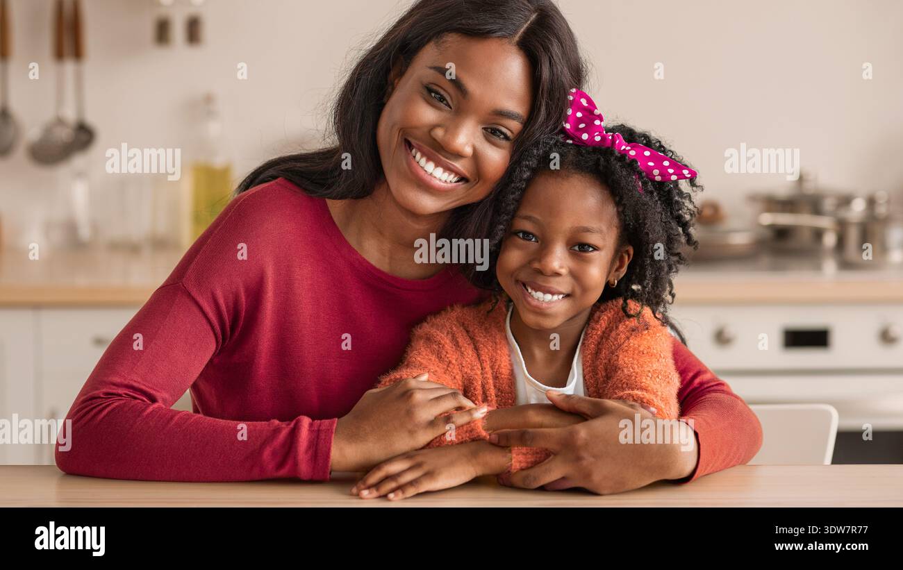 Madre e figlia condividono un momento di gioia mentre si siedono al tavolo della cucina durante il giorno Foto Stock
