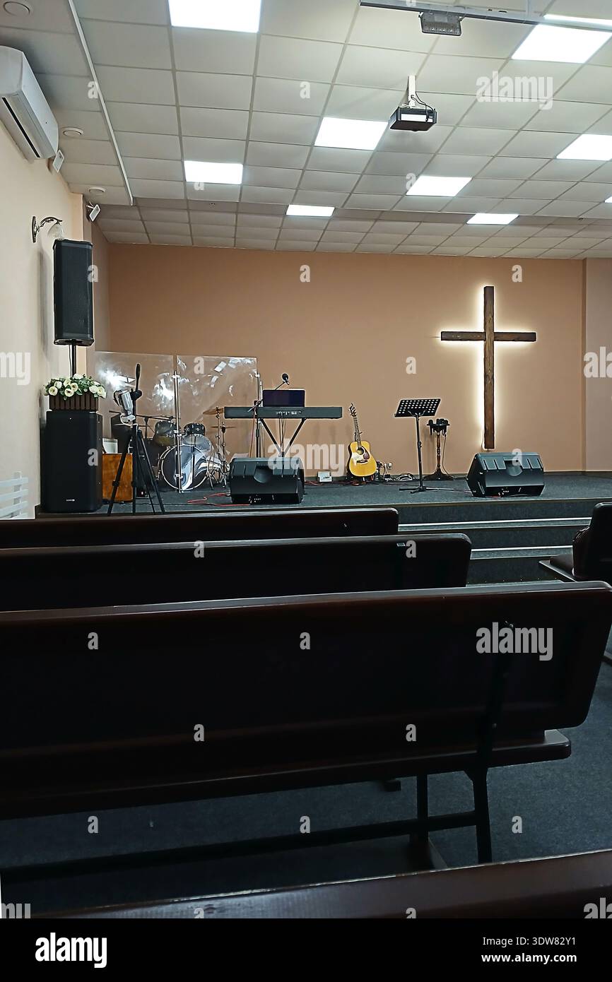Palco della chiesa vuoto con croce di legno, strumenti e panche pronti per il servizio di culto e la musica Foto Stock