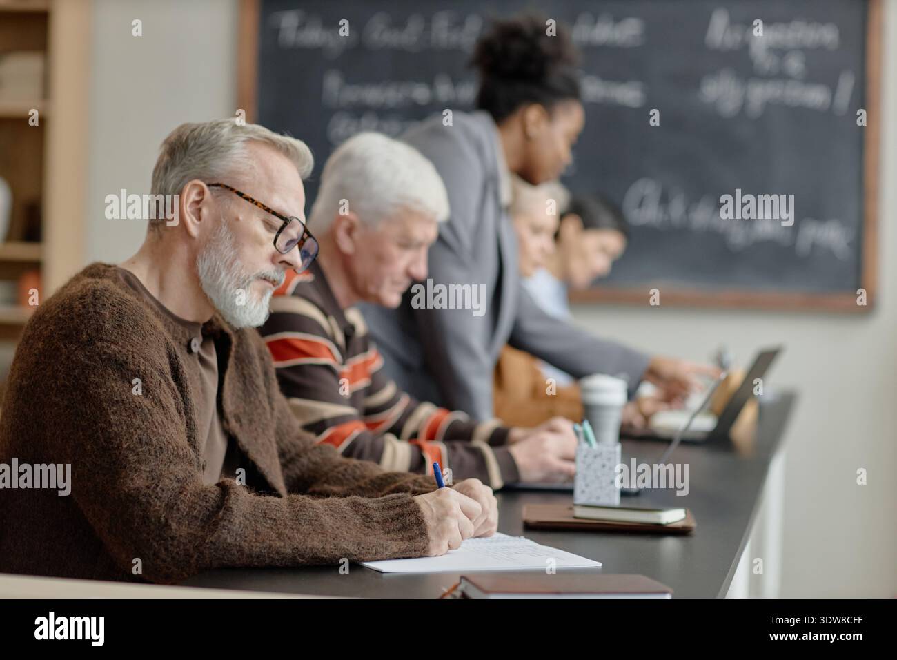 Uomini caucasici di mezza età che scrivono mentre studiano con diversi gruppi in classe Foto Stock