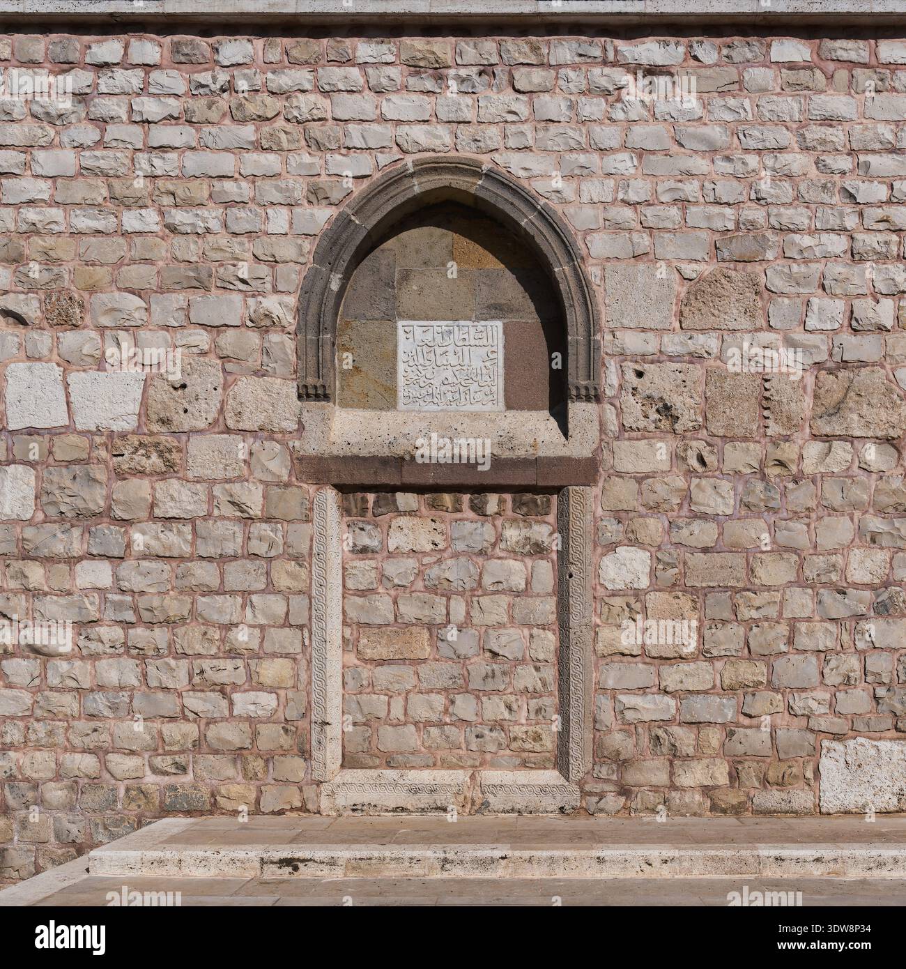 Vista dettagliata della parete esterna in pietra della Moschea di Alaeddin, Konya, Turchia, che mostra una nicchia ad arco con antiche iscrizioni arabe e intricate murature in pietra Foto Stock