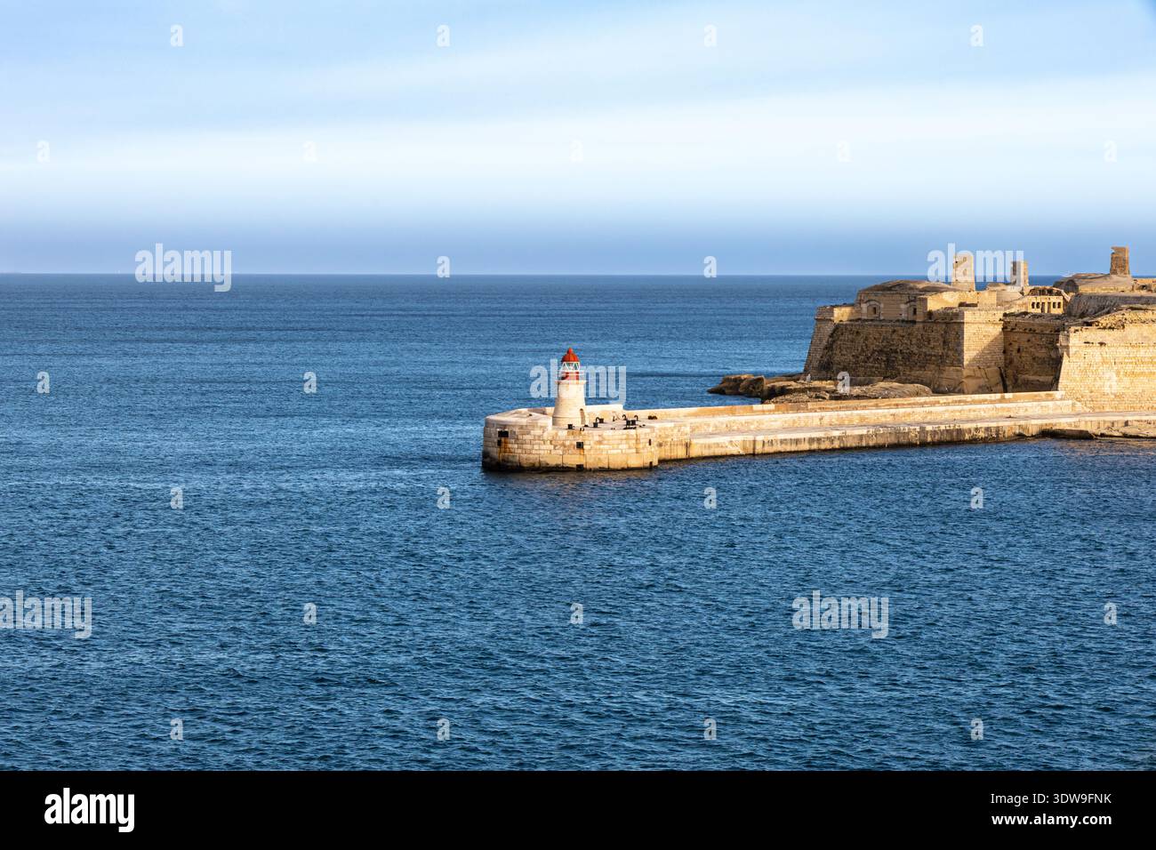 Un'ampia foto del faro di Sant'Elmo Breakwater e delle storiche fortificazioni in pietra contro il blu profondo del Mar Mediterraneo a Malta Foto Stock