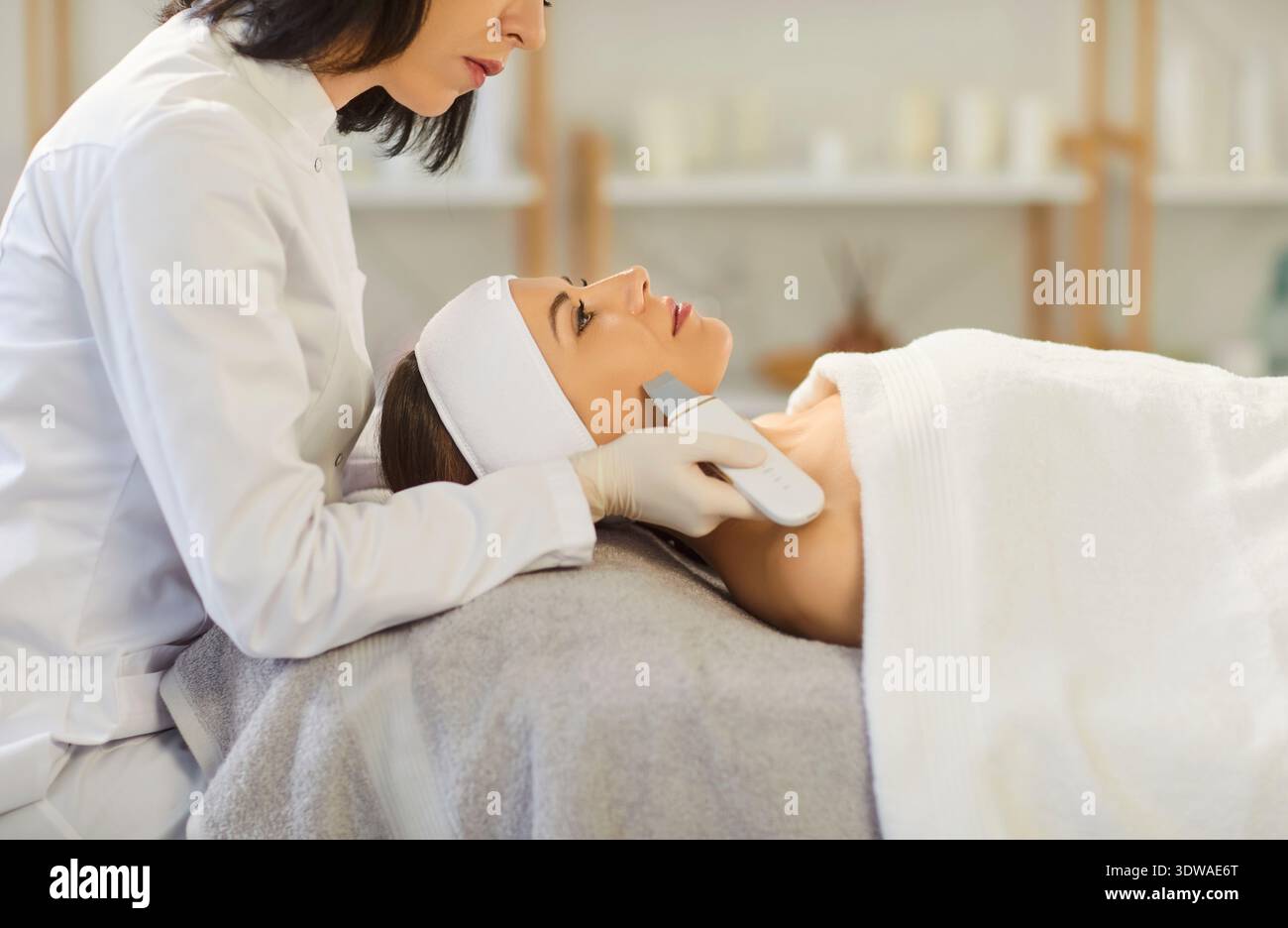Trattamento facciale effettuato da estetista utilizzando un dispositivo a ultrasuoni nella moderna clinica termale Foto Stock