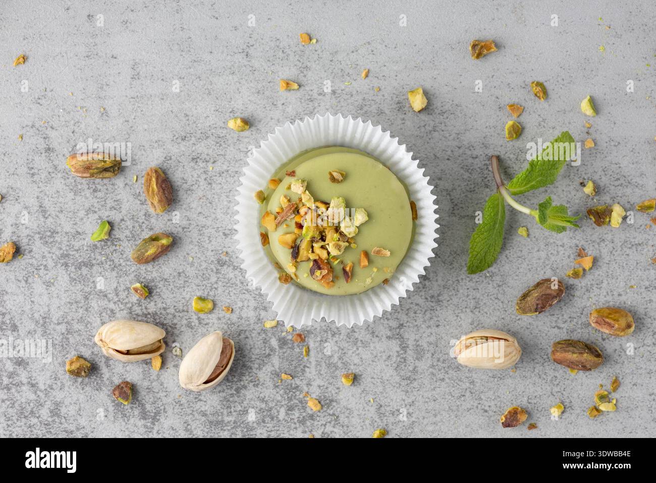 Torta mignon glassata verde con pistacchio tostato tritato e briciole su sfondo grigio in pietra. Dolce pasticceria di macaron. Foto Stock