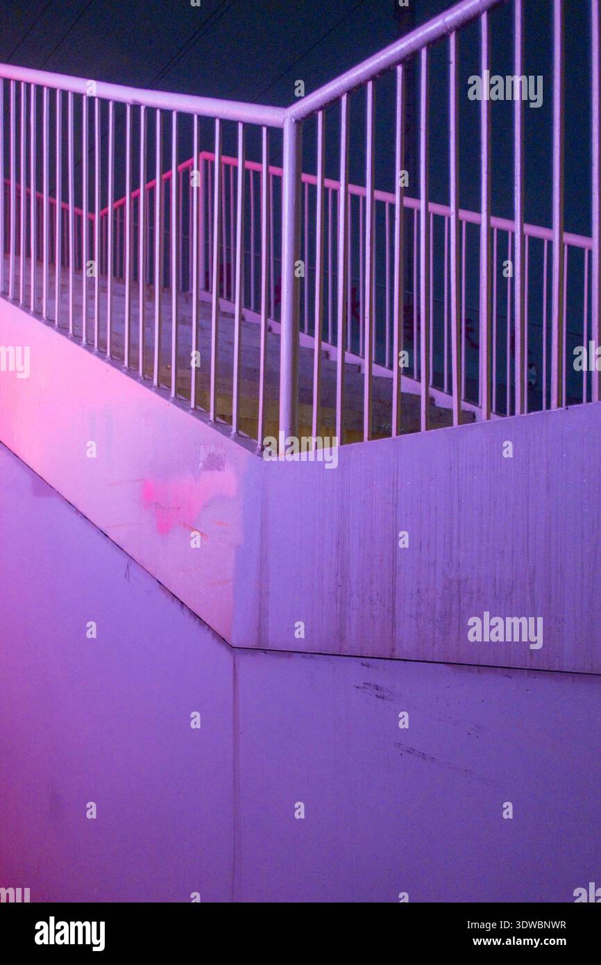 Una scala minimalista con ringhiera in metallo illuminata da una vivace illuminazione artificiale rosa e viola, che crea un'atmosfera architettonica futuristica Foto Stock