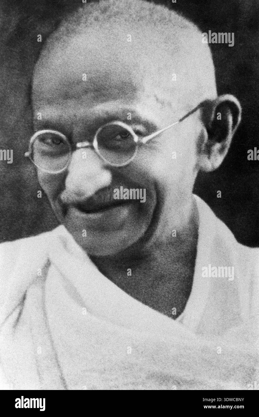 Un ritratto in primo piano, in bianco e nero di Mohandas K. Gandhi, che si ritiene risalga alla fine degli anni '1930 Si vede indossare i suoi caratteristici occhiali rotondi e il tradizionale abbigliamento indiano, con un sorriso debole sul viso, che trasmette un'espressione di gentile saggezza. Questa fotografia storica cattura il comportamento contemplativo dell'iconico leader. Foto Stock