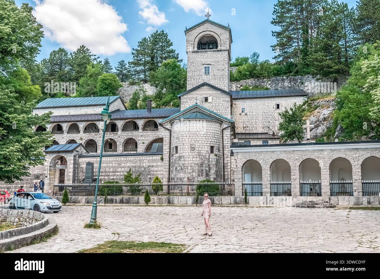 Un'auto bianca attraversa il complesso del monastero di Cetinje sulla piazza lastricata. L'immagine evidenzia il contrasto. Cetinje, Montenegro - 20 giugno 2021 Foto Stock