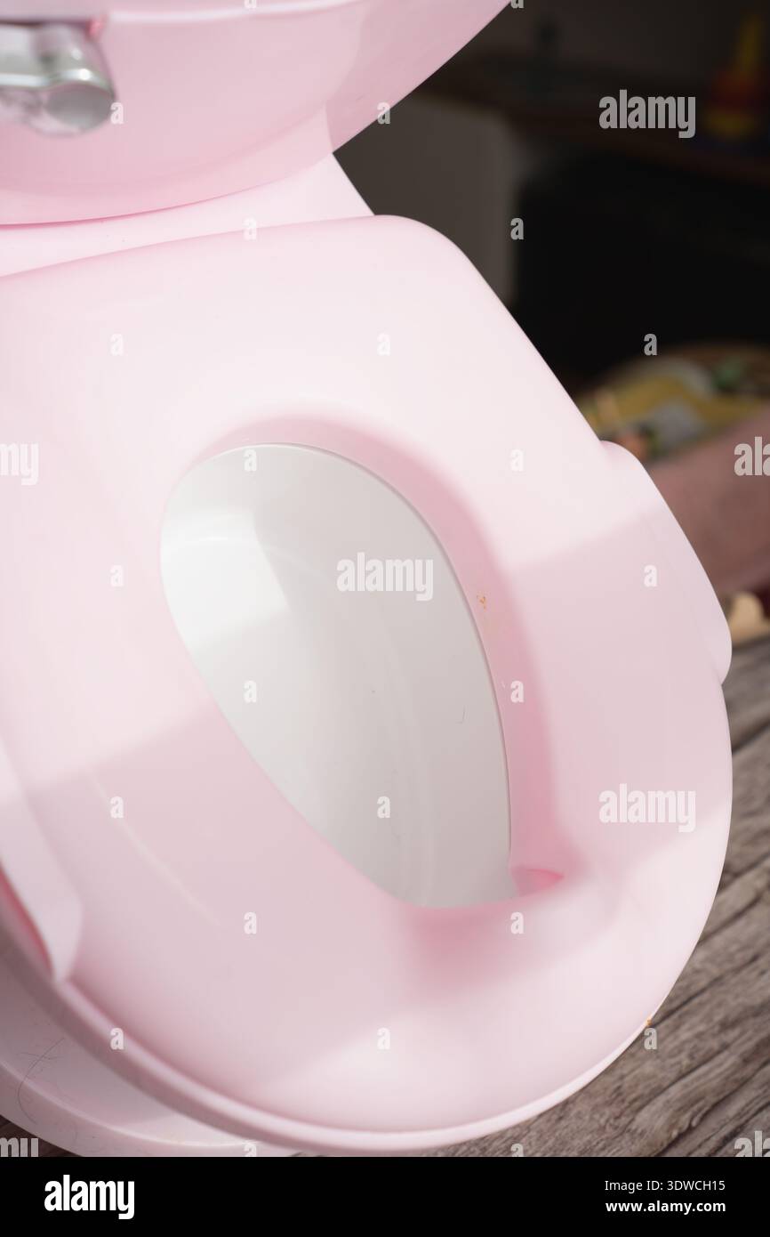 primo piano di un vasino in plastica rosa pastello con recipiente interno bianco aperto posizionato su una superficie in legno, luce soffusa e luminosa, forme curve lucide, delicato Foto Stock