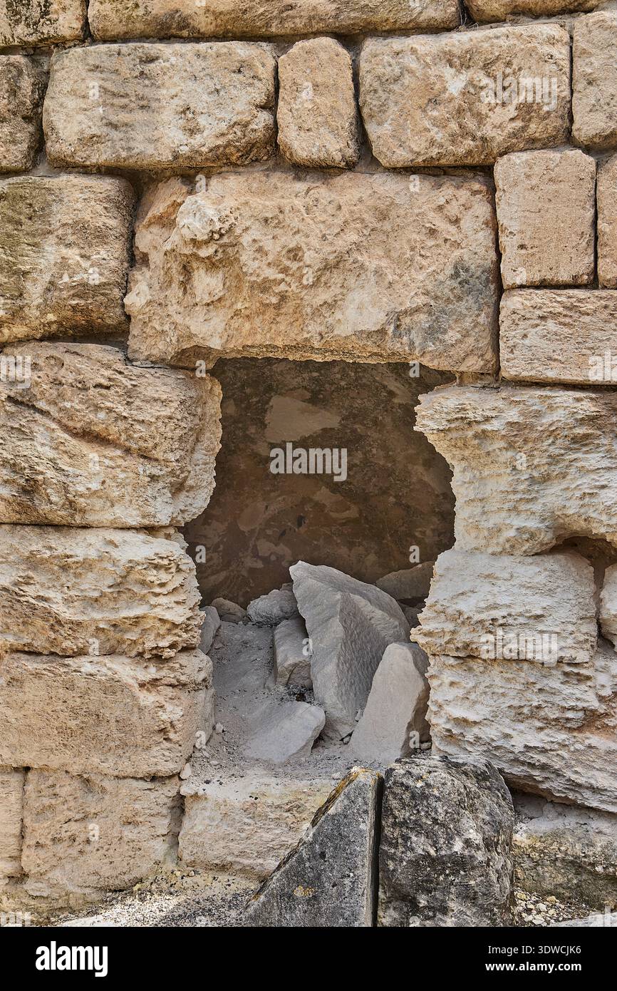 Antica parete in pietra con un'apertura rettangolare che rivela pietre rotte e detriti all'interno, mostrando texture intemperie e costruzioni storiche Foto Stock