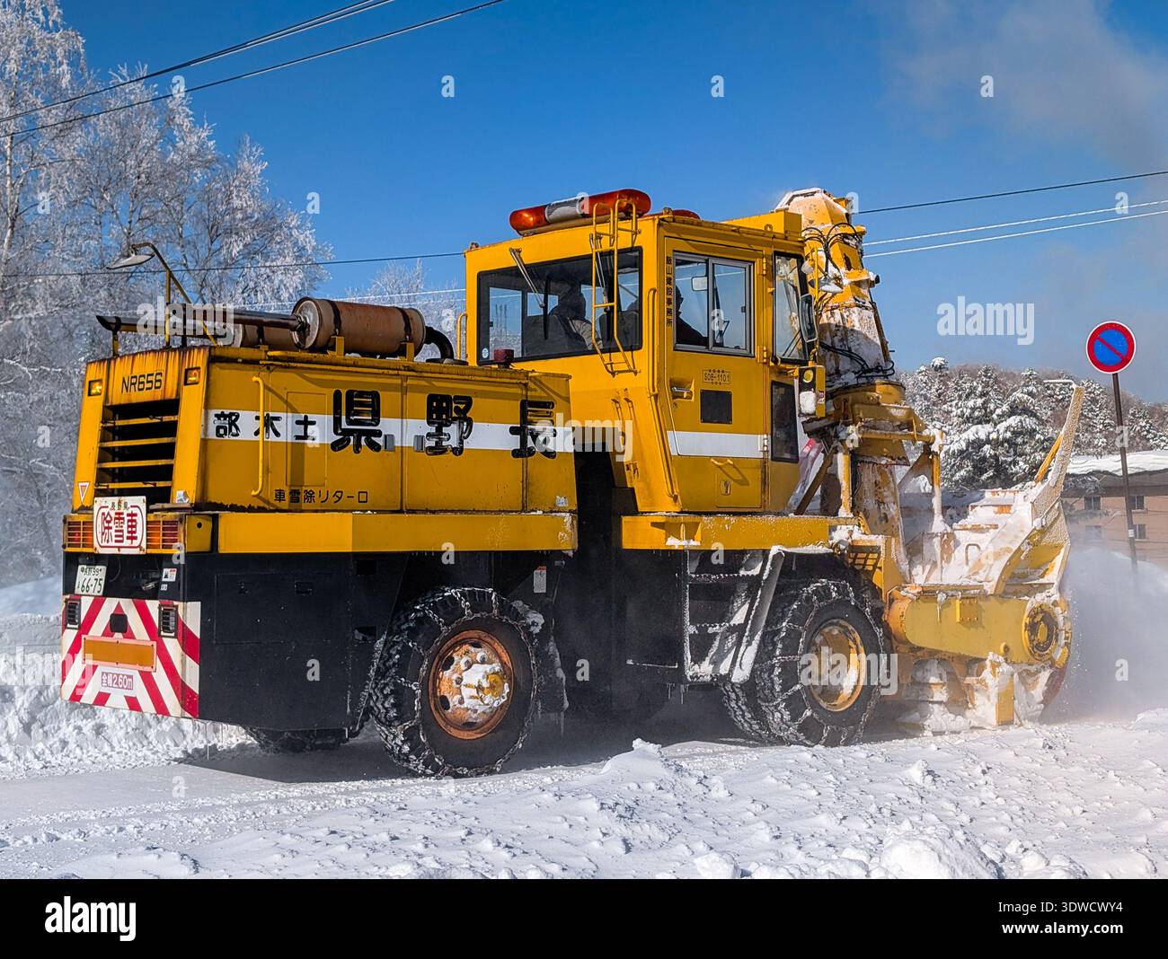 Grande veicolo giallo che soffia la neve fuori strada con alberi ghiacciati sullo sfondo Foto Stock