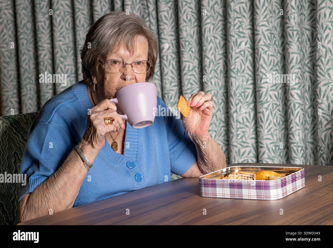 la nonna di 86 anni beve tè e mangia biscotti Foto Stock