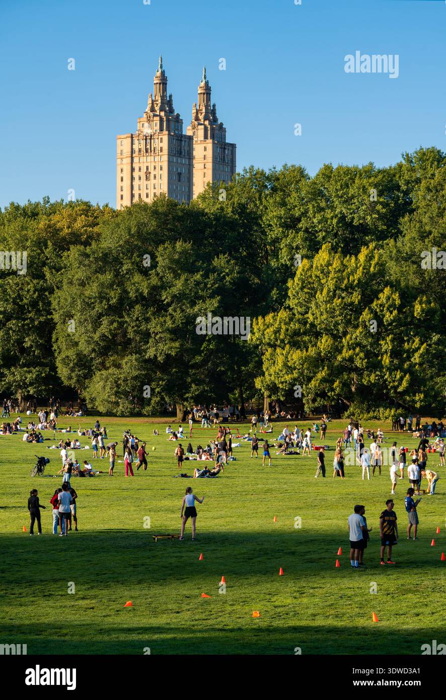 New York, Central Park. Le persone amano trascorrere un caldo pomeriggio estivo rilassandosi sul Sheep Meadow. Il San Remo sorge sopra la linea del Treeline nell'Upper West Side Foto Stock