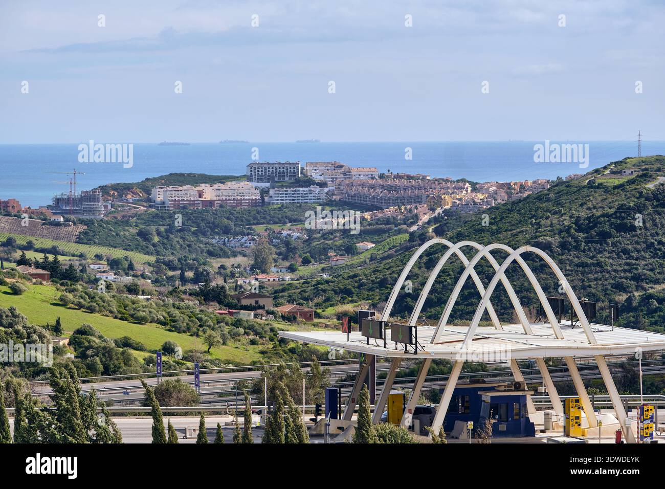 Manilva, Spagna - 18 febbraio 2026: Veduta delle case costiere che scendono lungo la collina verso il mare scintillante, incorniciate dagli eleganti archi del To Foto Stock