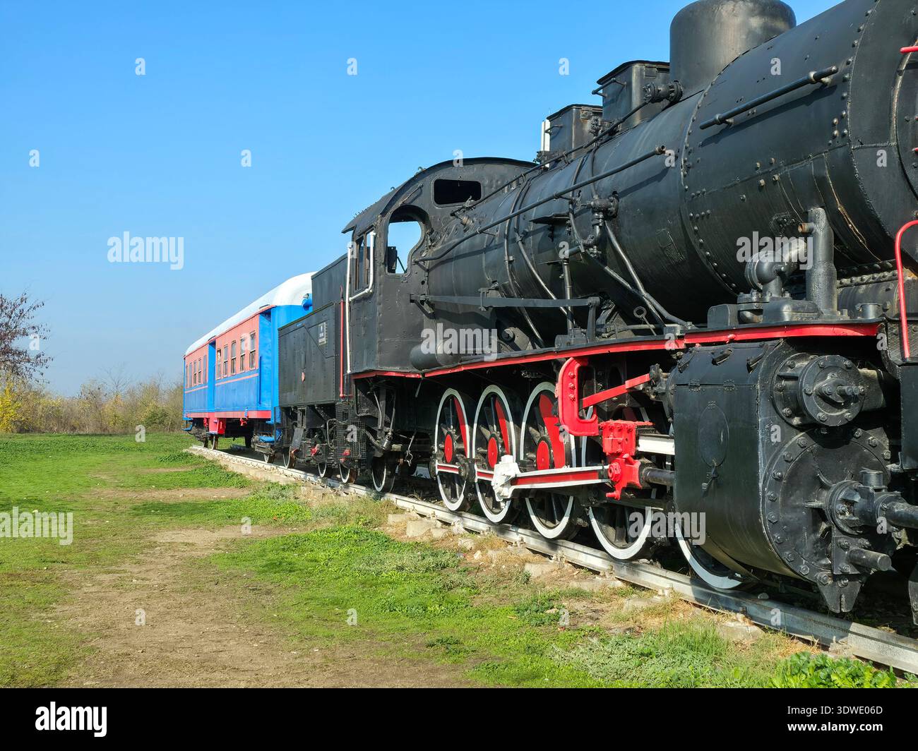 Una classica locomotiva a vapore nera con accenti rossi e un'autovettura blu su un binario ferroviario rurale. La scena cattura una vista nostalgica del treno trav Foto Stock