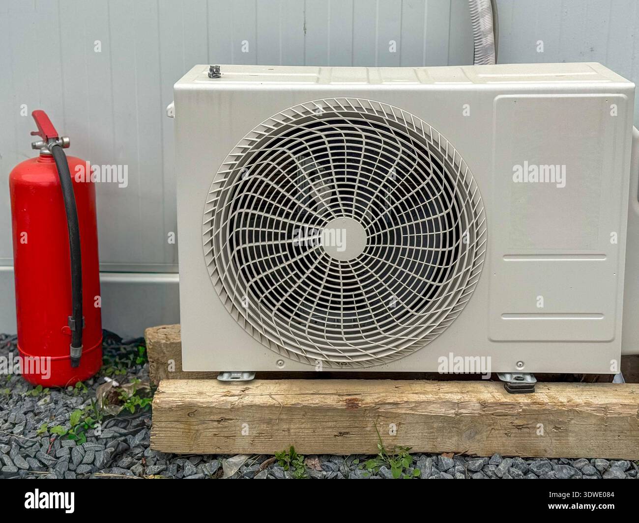 Condizionatore d'aria esterno posizionato su supporti in legno, accompagnato da un estintore rosso. La configurazione mette in evidenza sicurezza e funzionalità in un ou Foto Stock