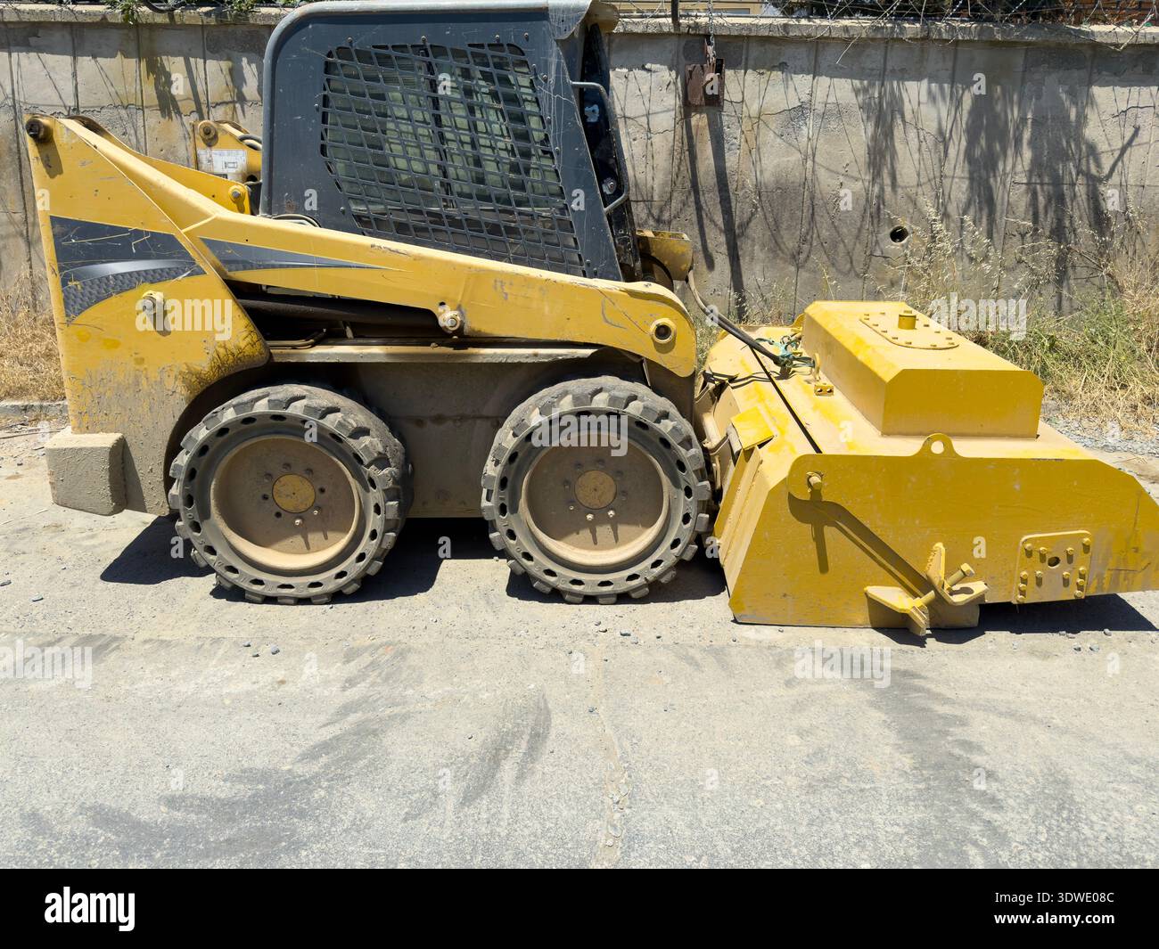 Una minipala compatta gialla con attrezzatura anteriore è parcheggiata in un cantiere. Il veicolo è dotato di pneumatici robusti, progettati per m. Foto Stock