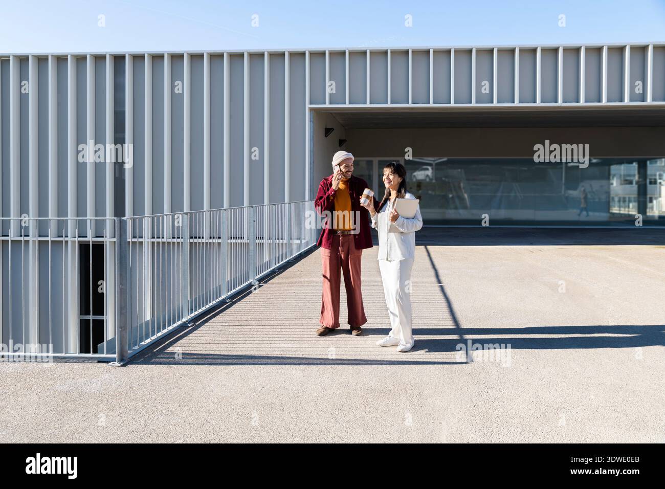 Due professionisti che hanno una conversazione fuori da un edificio moderno. Sembrano impegnati e amichevoli, in piedi in una giornata di sole, con la struttura Foto Stock