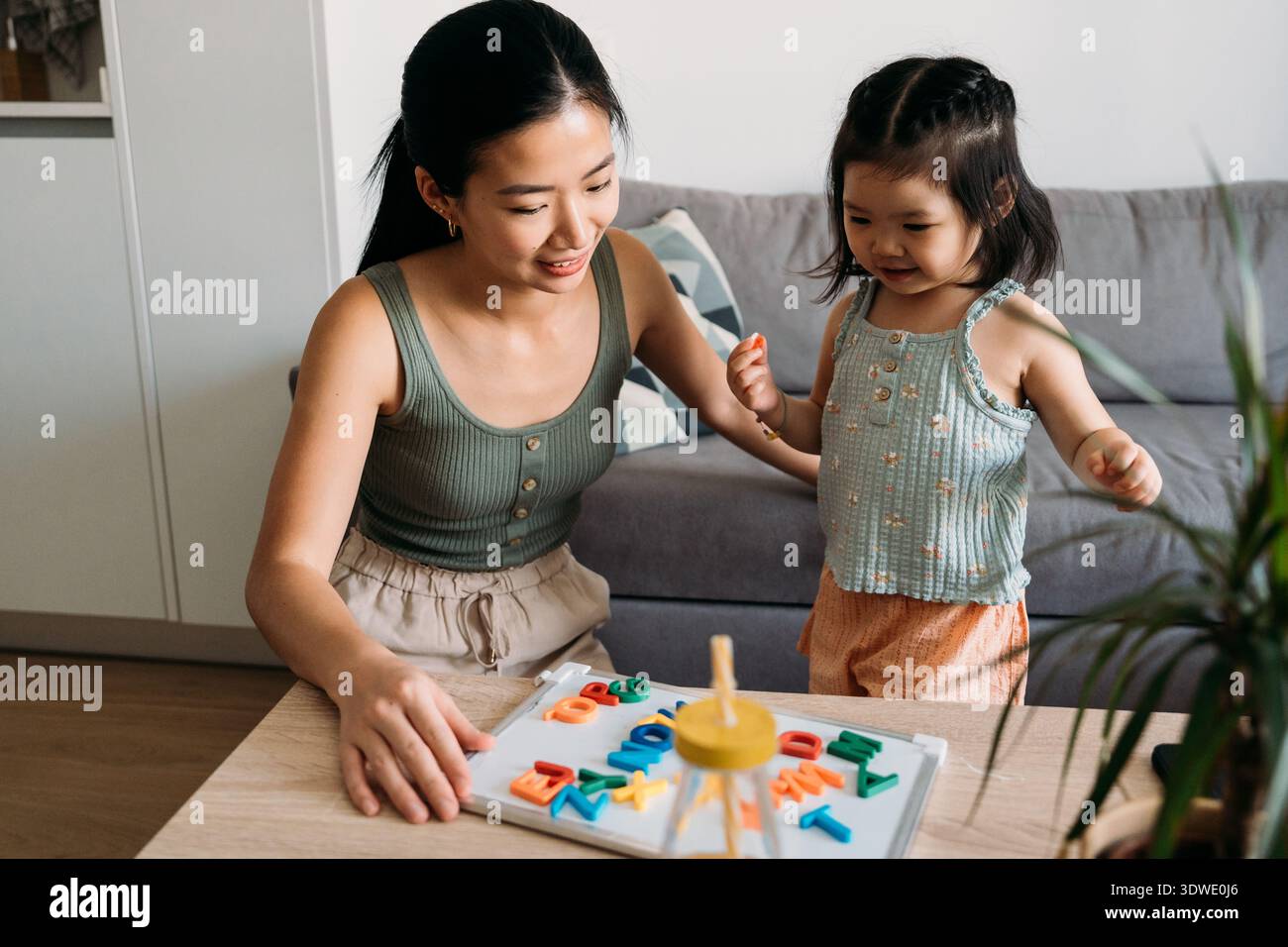 Una madre e una figlia si divertono a imparare giocando con i magneti colorati dell'alfabeto su un tavolo da cucina. L'interazione gioiosa migliora l'educ precoce del bambino Foto Stock
