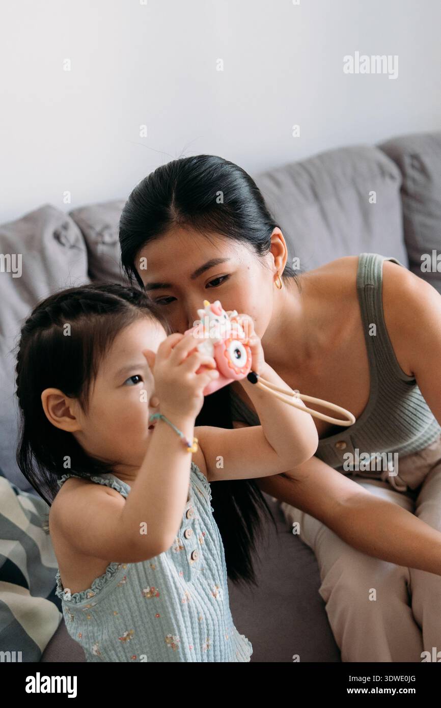 Una madre e suo figlio si divertono momenti divertenti insieme su un comodo divano. Il bambino ha in mano una macchina fotografica giocattolo, catturando ricordi preziosi nella loro intima atmosfera Foto Stock