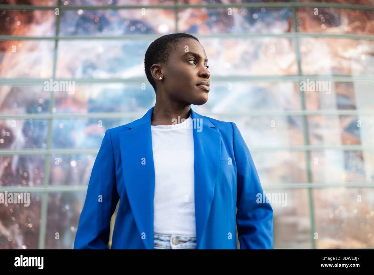 Una donna d'affari africana sicura di sé con una giacca blu si trova all'aperto. Il suo sguardo determinato suggerisce leadership e forza, incarnando le qualità di Foto Stock