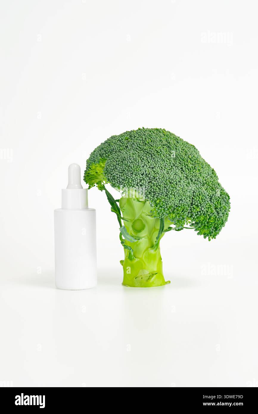 I broccoli freschi e una bottiglia di siero bianco vengono messi insieme, mostrando la miscela di alimenti biologici con cosmetici per la cura della pelle. Questa immagine evidenzia il natur Foto Stock