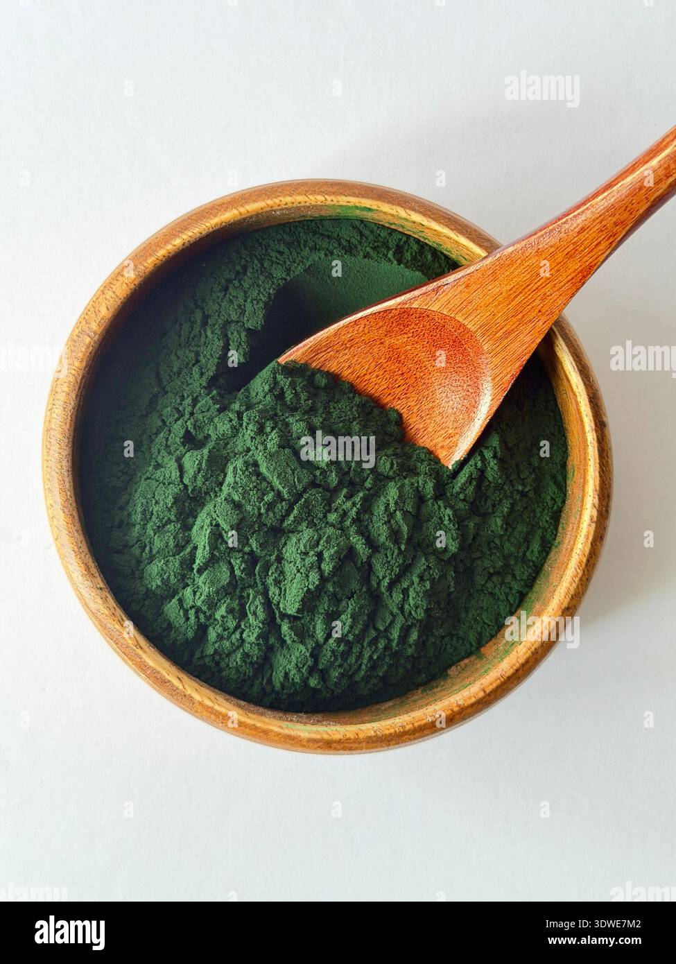 Polvere di spirulina organica in recipiente di legno con cucchiaio su sfondo bianco. Alghe superfood ricche di sostanze nutritive, perfette per disintossicazione, frullati e benessere. - Immagine stock catturata con smartphone