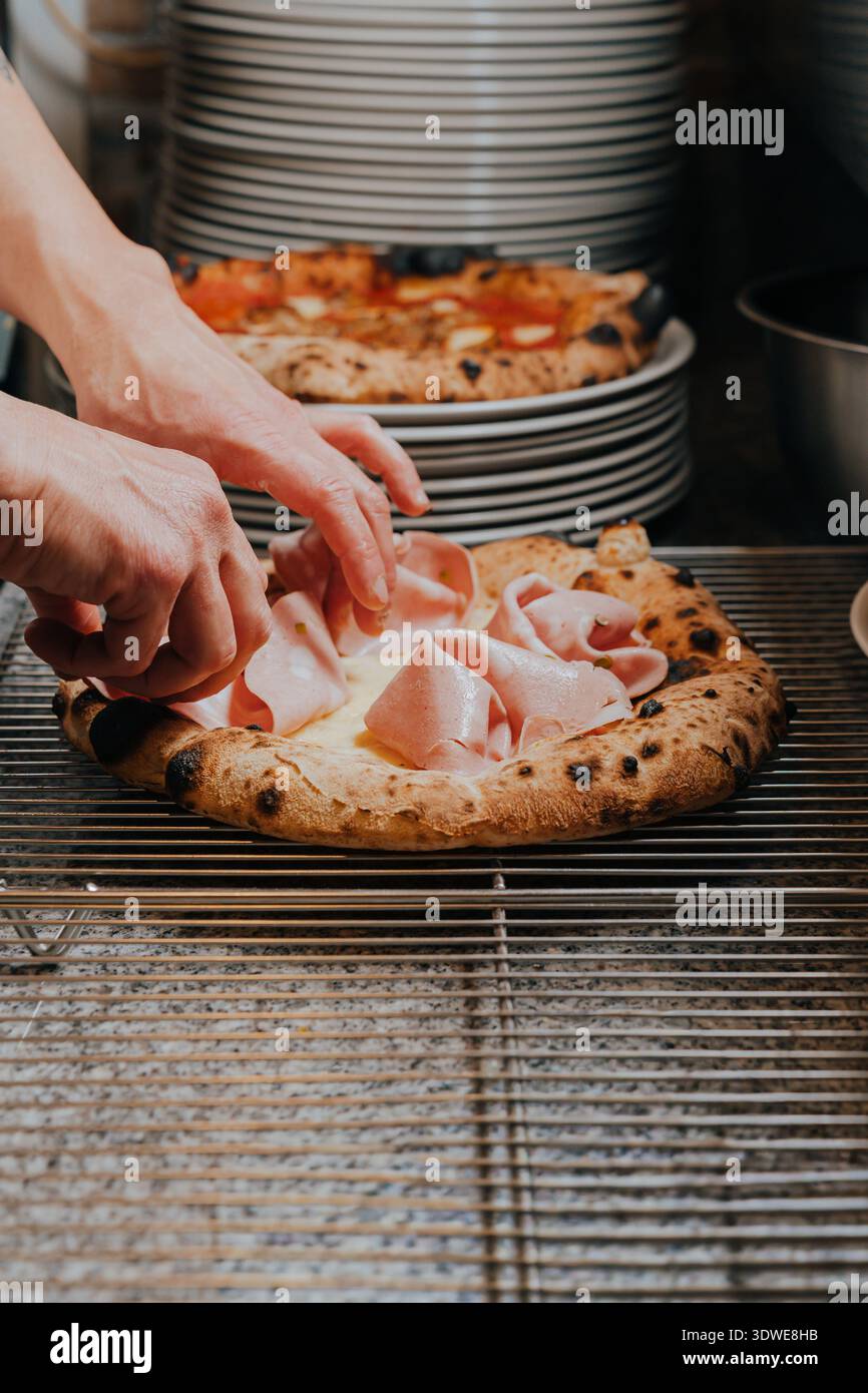Uno chef esperto mette delicatamente ingredienti freschi su una pizza in una tradizionale pizzeria napoletana. L'immagine cattura l'essenza dell'autentica, maneggevole Foto Stock