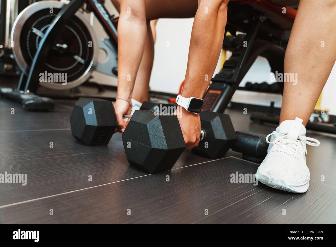 Donna che solleva due manubri in palestra, concentrandosi sull'allenamento di forza e sul fitness. L'immagine enfatizza uno stile di vita sano e la dedizione. Foto Stock