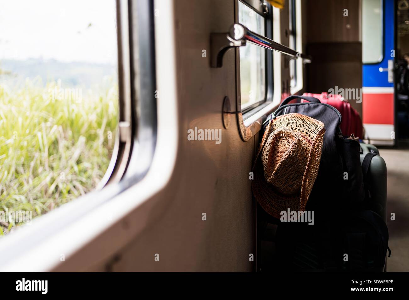Un accogliente compartimento ferroviario in Sri Lanka, adornato con bagagli e un cappello di paglia. La luce del sole scorre attraverso la finestra, evidenziando il lussureggiante terreno verde Foto Stock