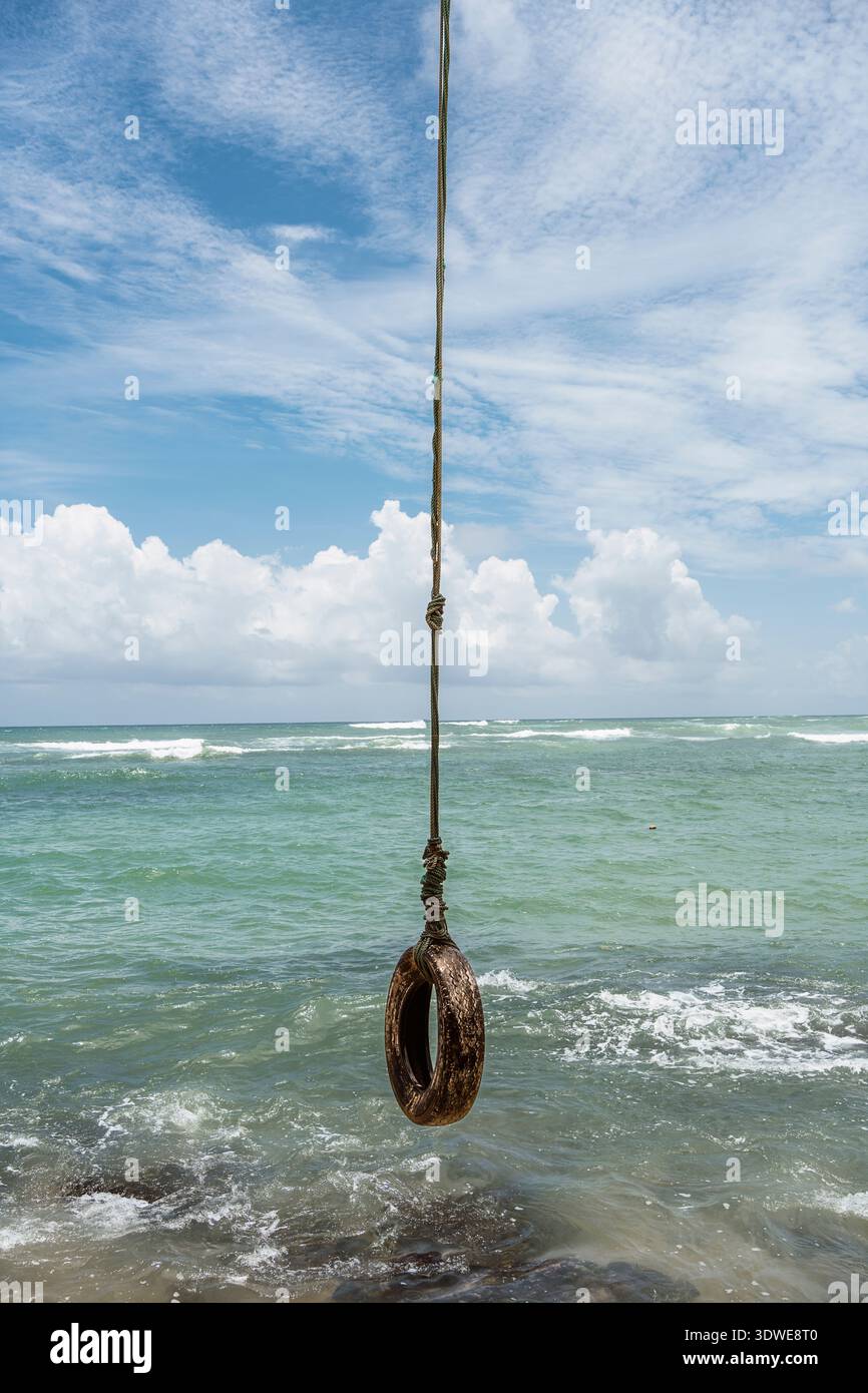 Un rustico dondolo di gomme pende sulle dolci onde dell'oceano in Sri Lanka, offrendo un nostalgico assaggio del divertimento sul mare. L'impostazione presenta una b chiara Foto Stock