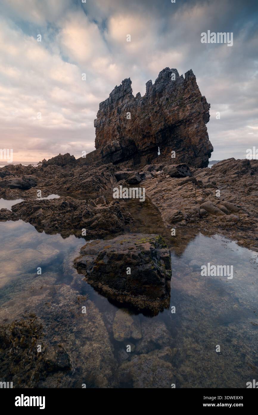 L'aspra bellezza di Playa Portizuelo nelle Asturie, Spagna. Il nuvoloso cielo estivo getta uno sfondo suggestivo sulle formazioni rocciose uniche e sul mare tranquillo Foto Stock