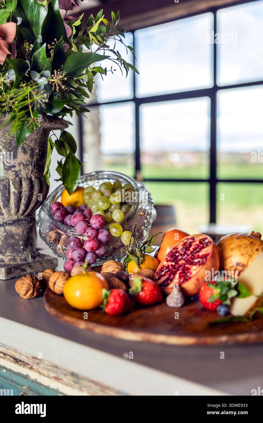 Un vivace spettacolo di frutta assortita come fragole, mirtilli, uva e melograni, abbinato a noci e formaggi su un tavolo rustico. Foto Stock