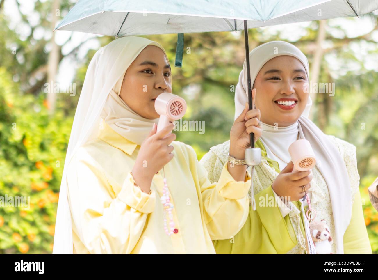 Due donne musulmane che indossano hijab sono viste all'aperto mentre girano un video musicale. Possono contenere ventilatori portatili e un ombrello, coinvolgendo in modo creativo un li Foto Stock