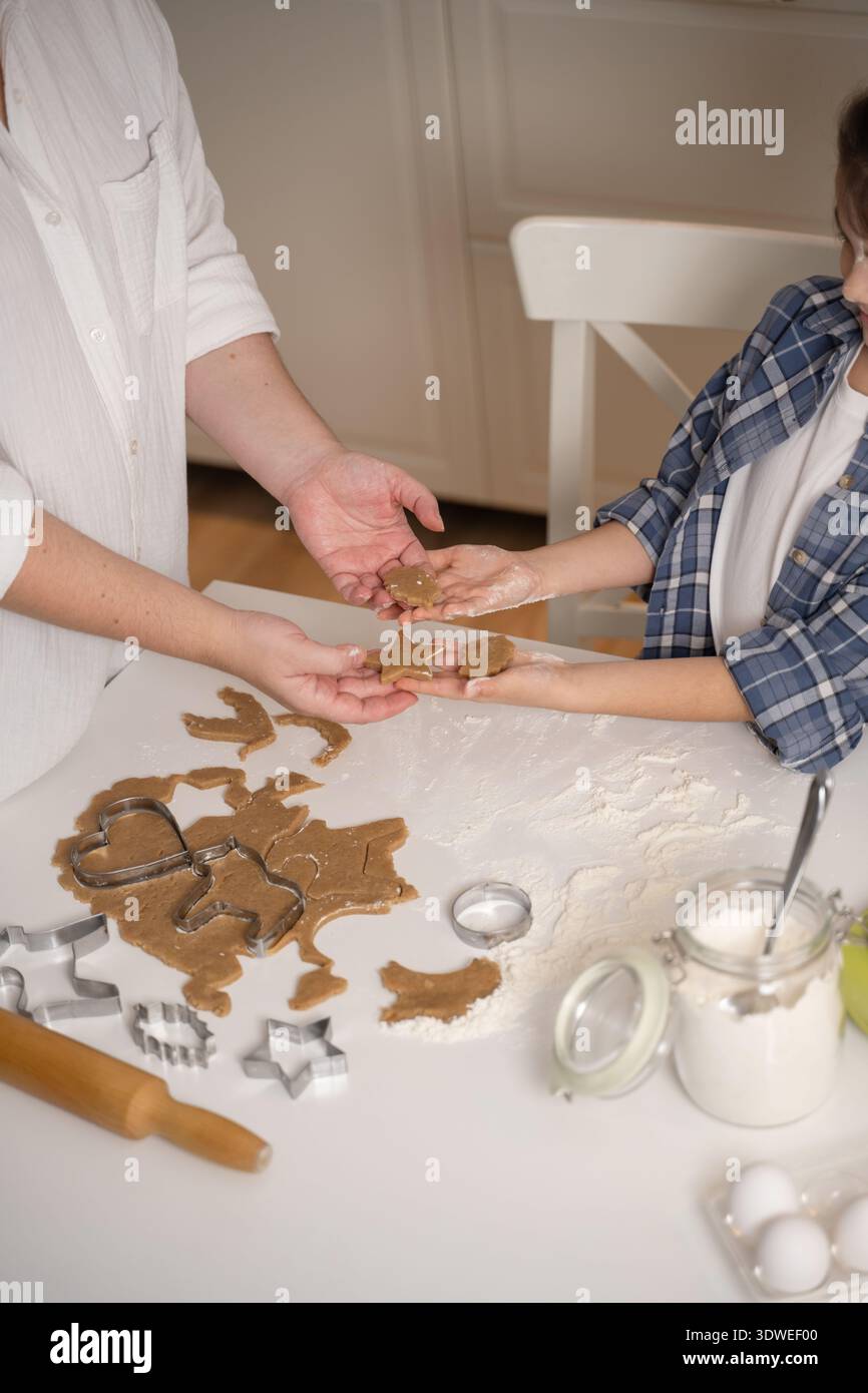 Una madre e una figlia si divertono a cucinare biscotti insieme a casa. Condividono uno speciale momento di incollaggio, passando l'impasto tra i due Foto Stock